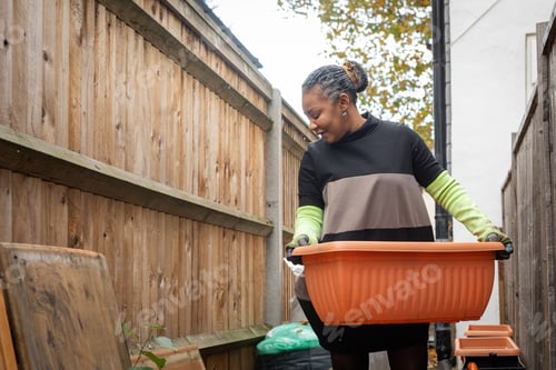 Preview: Woman Living With Hiv Carrying A Gardening Tub Outside Of Her Home In London
