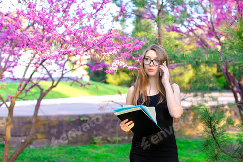 Preview: Beautiful Businesswoman Talking With Partner By Smartphone Near Trees In Blossom And Keeping Black
