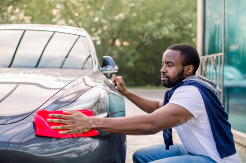 Preview: Young African Man Washing And Wiping His Modern Blue Gray Car Headlight At The Outdoor Car Wash