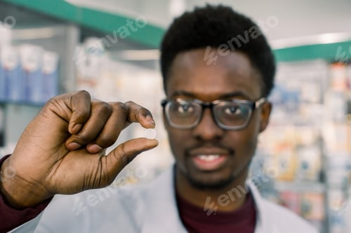 Preview: Young Smiling African-American Doctor Pharmacist Man Holding White Tablet Pill In The Hand