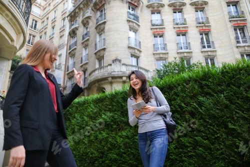 Preview: Cheerful Blonde Girl Talking With Chinese Female Person Keeping Tablet And Shaking Hand In