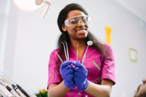 Preview: Dental Concept. Pretty Female Dentist In Pink Suit, Protective Glasses And Blue Latex Gloves Shows