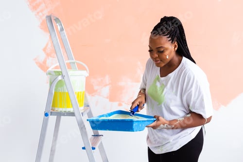 Preview: Young Happy African American Woman Painting Interior Wall With Paint Roller In New House. A Woman
