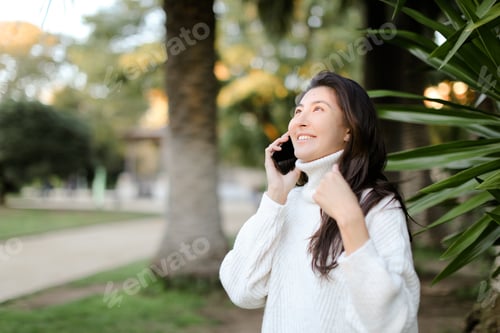 Preview: Chinese Happy Girl In Tropical Park Talking By Smartphone Near Palm. Concept Of Modern Techology