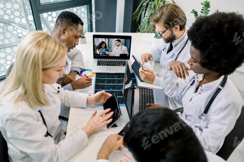 Preview: Multiethnic Doctors Making Notes On Laptop And Tablets During Video Call At Hospital, Chatting With