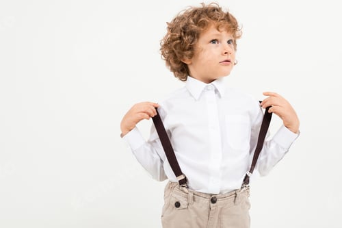 Preview: Charming Boy With Curly Hair In White Shirt With Black Suspenders Stands Isolated On White