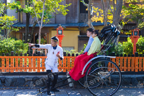 Preview: Kyoto, Japan - November, 8, 2019: Japanese Trishaw Amuses Mature Asian Couple Sitting In Rickshaw