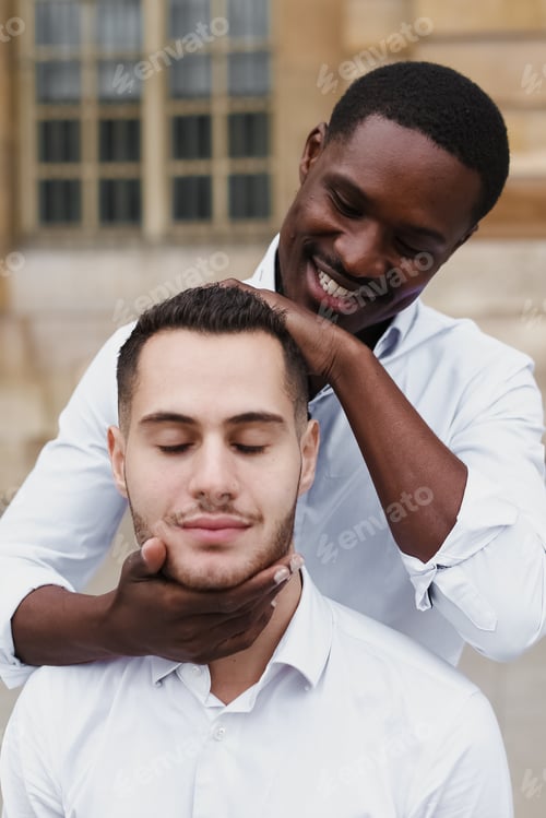 Preview: Afro American Boy Holding Caucasian Guy Head By Hands, Wearing White Shirt. Concept Of Stylish Boy