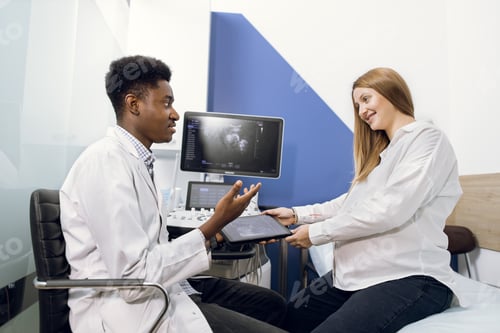 Preview: Doctor And Patient In Ultrasound Room. African Male Doctor Talking To His Young Pregnant Woman