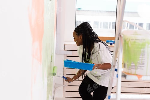 Preview: Young Happy African American Woman Painting Interior Wall With Paint Roller In New House. A Woman