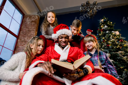 Preview: Santa Claus Reads An Ancient Book With Christmas Stories For Children Sitting Around A Red Chair