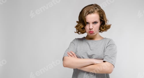 Preview: Charming Young Girl In A Gray T-Shirt On A Gray Background. The Girl Folded Her Arms Over Her Chest