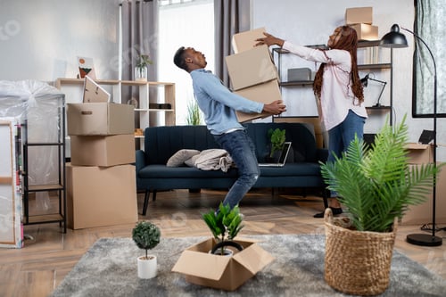 Preview: Young African Couple In Casual Clothes Packing Boxes For Moving To New House. Concept Of Real