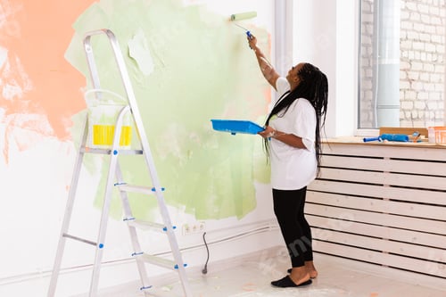 Preview: Beautiful African American Girl Painting The Wall With Paint Roller. Portrait Of A Young Beautiful
