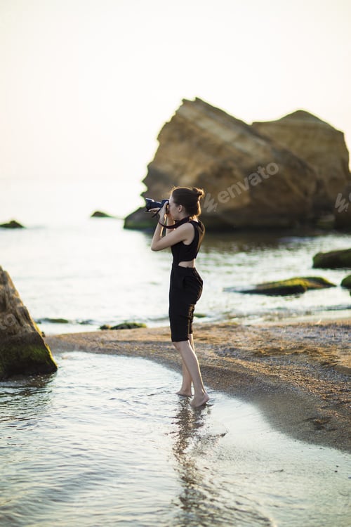 Preview: Young Woman Photographer Holding Camera And Looking Into Frame. Girl Dressed In Black Jumpsuit