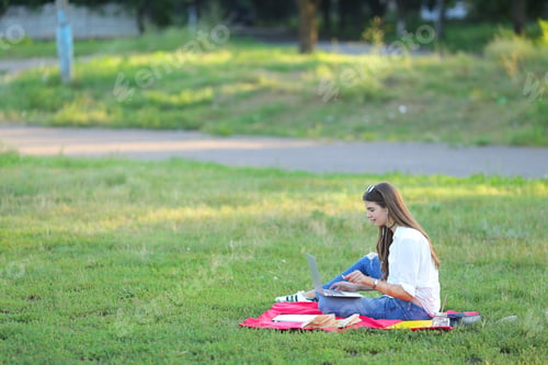 Visualização: Jovem sentada no parque e falando com fones de ouvido no Skype através do notebook. Estudante