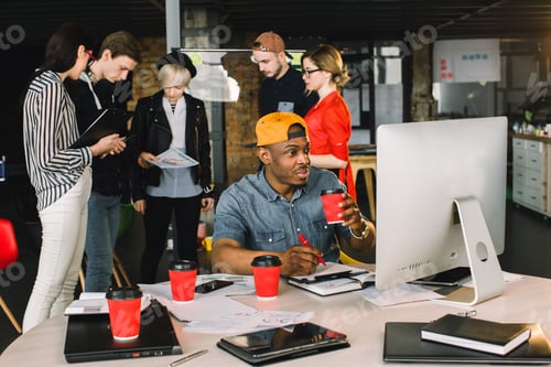 Preview: Smiling Young African Man Drinking Coffee While Sitting At The Table And Using Computer In Modern