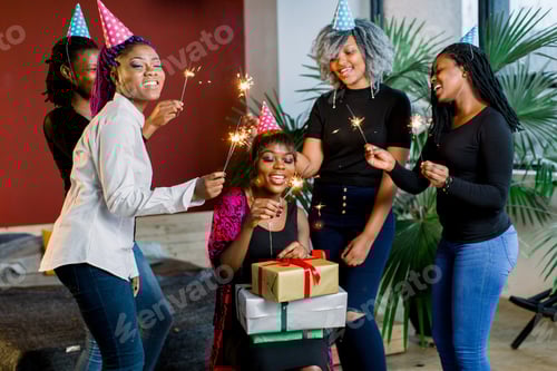 Visualização: Amigos africanos comemoram aniversário segurando luzes de Bengala e com chapéus e presentes