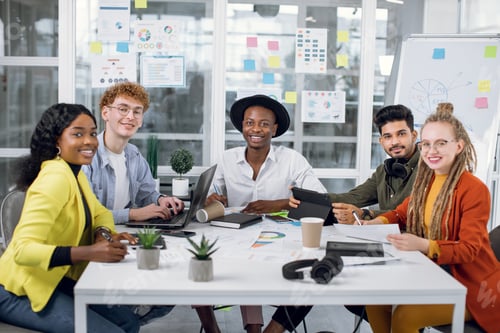 Preview: Smiling Five Multiracial Young Students In Stylish Outfit Looking At Camera While Sitting At Office