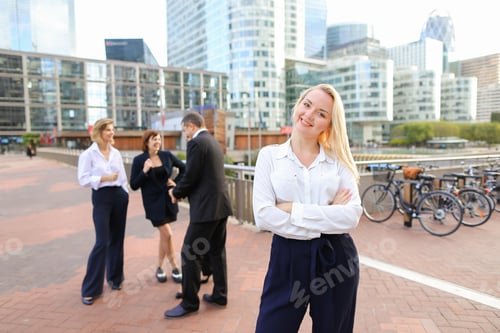 Preview: Blonde Secretary Looking At Camera And Playing With Hair Near Talking Employees Background. Concept