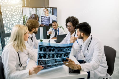 Preview: Online Medical Video Conference In Bright Room, With A Tv Screen. Multiracial Doctors Sitting At