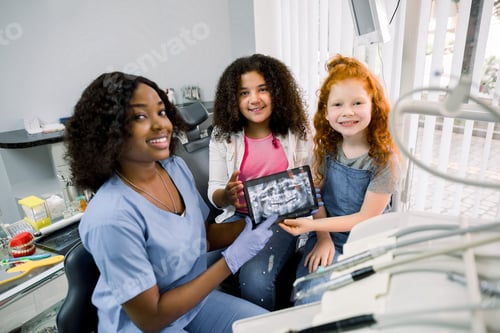Preview: Shot Of Professional Female African Dentist And Her Two Little Patients, Multiethnic Shcoolgirls