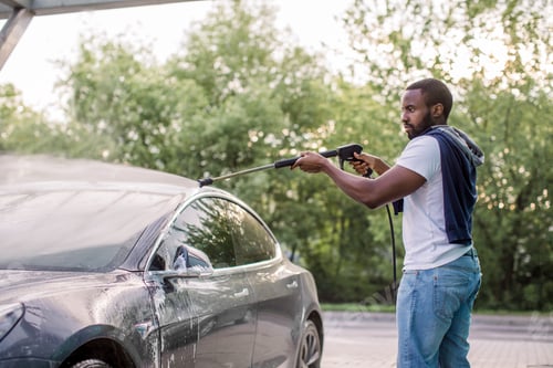 Preview: African Stylish Young Focused Man In Casual Clothes Washing His Modern Electric Car With A Water