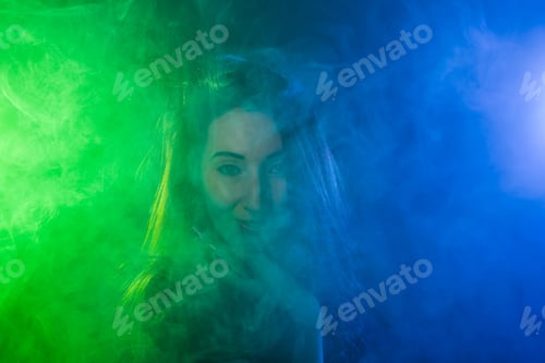 Preview: Portrait Of Young Woman In Neon Blue And Green Smoke With Vape Or E-Cigarettes