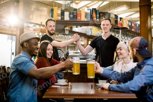 Preview: Happy Multiethnical Friends Having Drinks In A Bar, They Are Sitting At A Wooden Table With Beers