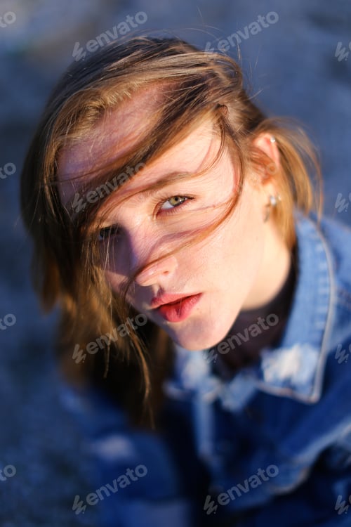 Preview: Cute Girl With Serious Facial Expression Posing On Camera Putting Hair On Face Against Blue Sea And