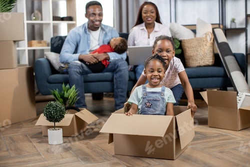 Preview: Two Cute Little Girls Kids Playing With Cardboard Boxes At New Apartment. Afro American Parents