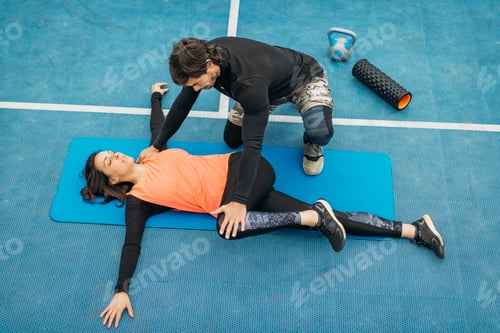 Preview: Woman receiving assisted stretch from trainer outdoors
