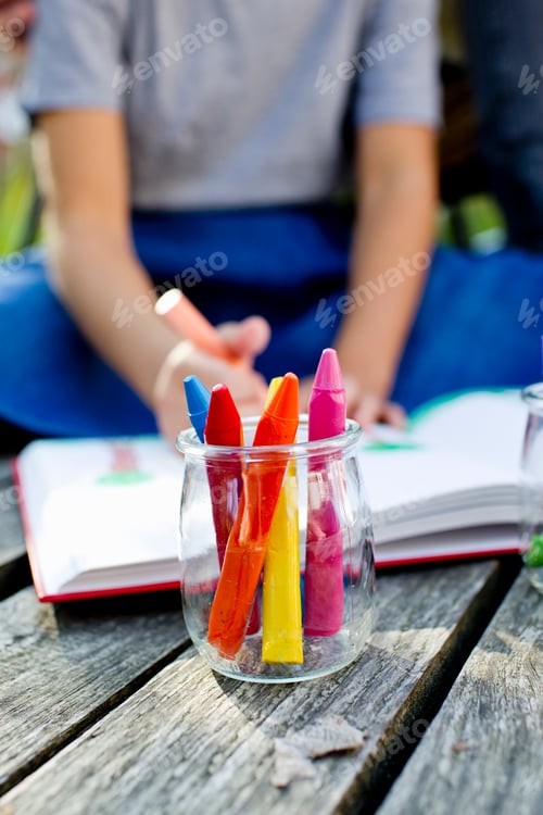 Preview: Jar of crayons close up with girl in background