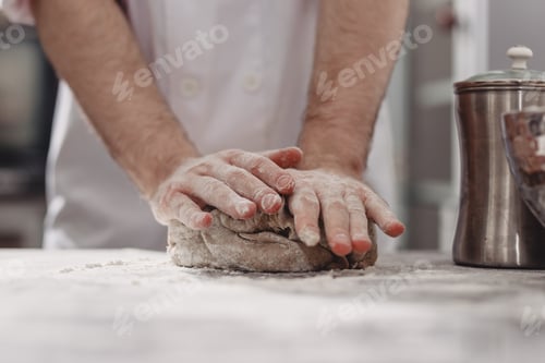 Preview: Professional baker kneads dough on the table in the kitchen of the bakery