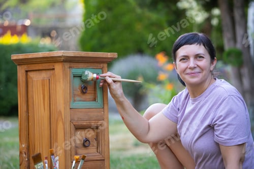Preview: Woman painting a wooden furniture outdoors, an eco-friendly re-use business.