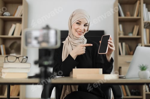 Preview: Woman filming video on modern phone camera while opening parcel box with new smartphone