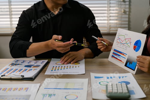 Preview: Business people analyzing financial charts and graphs using pens at office desk