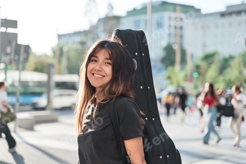 Preview: portrait of a young music student walking with guitar case on her back