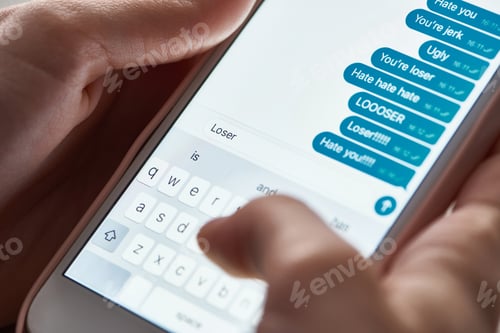 Preview: partial view of abuser sending offensive messages while using smartphone, illustrative editorial