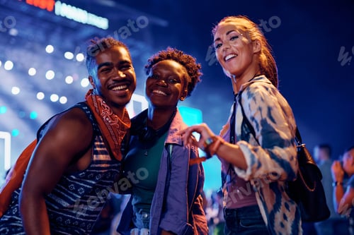 Preview: Group of happy festival goers in front of music stage at night looking at camera.