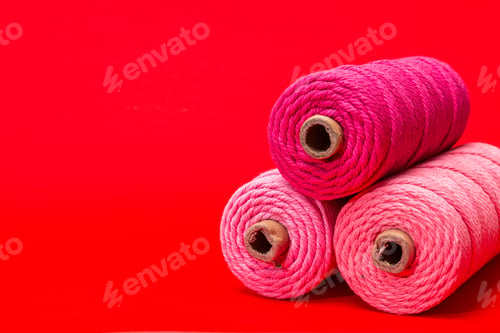 Preview: Close-up of Pink and Red Spools of Thread on Red Background Textile