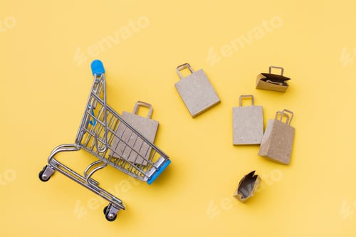 Preview: Eco-friendly craft paper bags in and near a metal shopping cart on a yellow background.