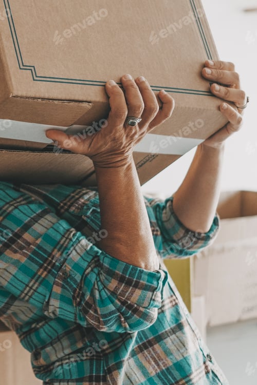 Preview: One woman lifting up heavy cardboard box during relocation moving house activity alone. Mortgage.