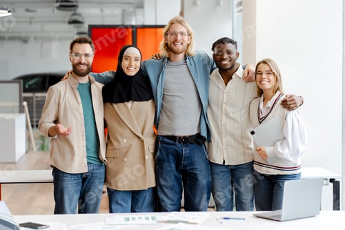 Preview: Diverse multiracial team of five business people hugging posing in the office, looking at camera