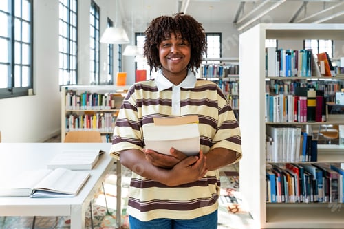Preview: Smiling student holding books in university library