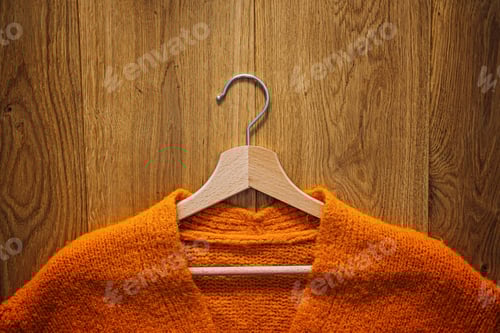 Preview: Orange Sweater on Wooden Hanger and Wooden Background