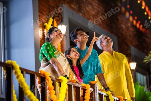 Preview: Indian family celebrating Diwali, with a young girl pointing at fireworks in the night sky