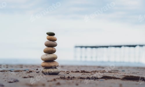Preview: Pebble tower by the seaside with blurry pier down to the sea, Stack of zen rock stones on the sand,