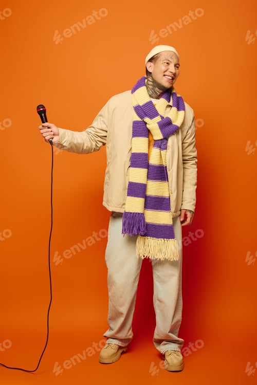 Preview: A young man with tattoos joyfully performing with a microphone on a vibrant orange backdrop