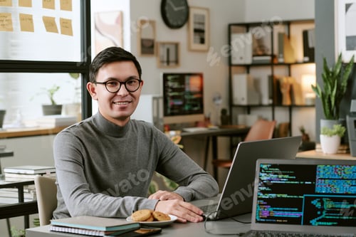 Preview: Portrait of Young Adult Asian Man Smiling While Working on Laptop in Office